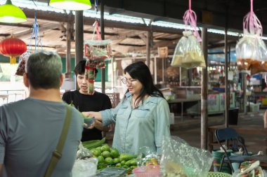 İki LGBTQ arkadaşı canlı bir Tayland pazarından taze sebze alıyor. Biri elinde bir sepet tutarken, diğeri meyveleri topluyor ve keyifli bir anı paylaşıyor. Onları çevreleyen canlı bir pazar ortamı var..