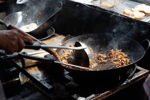 Şef sıcak tavada et ve sebzeleri karıştırıyor sokak yemeklerinde yükselen buharla geleneksel Asya yemek pişirme sürecini ve otantik yerel mutfak hazırlıklarını durduruyor