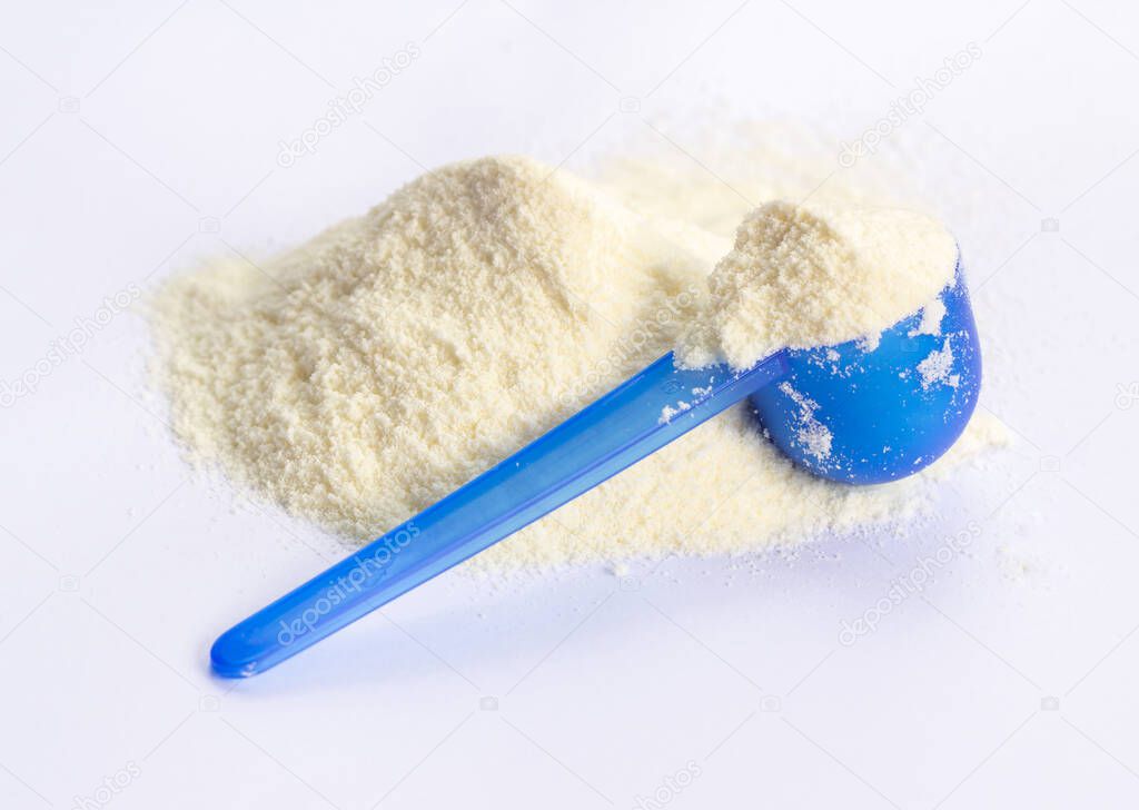 Dairy or milk powder for children heap on a white isolated with blue plastic spoon, formula is as gentle as a baby food. Newborns or as a health supplement