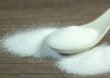 Yemek pişirmek için masa tahtasında beyaz kaşık içinde şeker beyazı granüle kristaller..