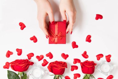 Sevgililer Günü için hediye kutusunu kadın elleri tutuyor. Beyaz arka planda kırmızı güller ve mumlar.