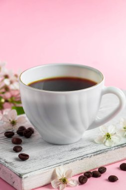 Bir fincan koyu espresso kahve ve pembe arka planda narin bahar çiçekleri. Bahar ve günaydın konsepti.