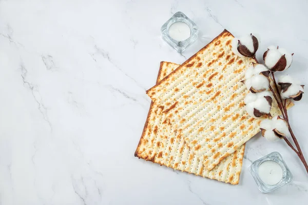 Happy Passover concept. Matzo bread and cotton flowers on white marble. Background religious Jewish holiday Pesach. Copy space.