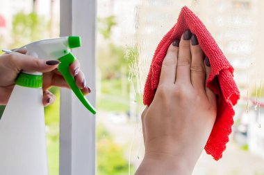 Cam temizleme ve ev temizliği. Genç bir kadın bardağa deterjan püskürtüyor. Ev işi kavramı.