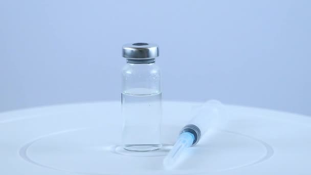Injekční roztok a injekční stříkačka na bílém pozadí. Ampulka s vakcínou se otáčí na stole. Koncepce očkování populace. — Stock video