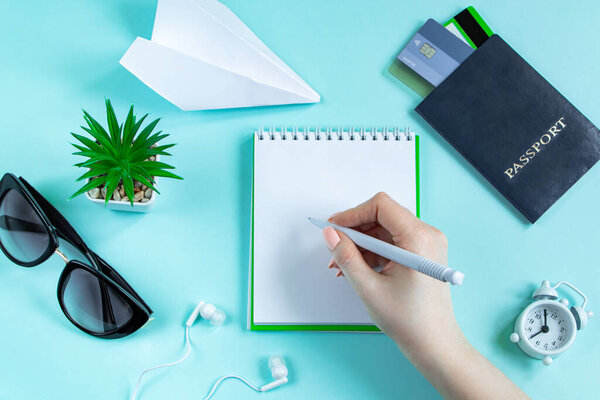 Женщина планирует летние каникулы. Туристические аксессуары на синем фоне. Паспорт, солнцезащитные очки и блокнот. Флэтли.