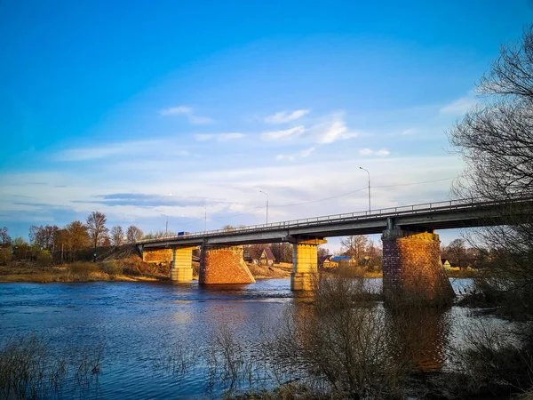 The ancient bridge over the river with stone pillars. Rapid flow of water in spring. Sunset view.