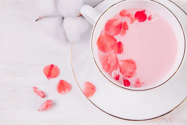 Trendy vegan tea on a white background. Pink matcha with rose petals in a cup. Relaxing drink recipe for sleepy times.