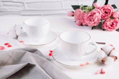 Kahve için iki boş beyaz fincan ve bir buket gül. Sabah kahvaltısı için iki kişilik masa..