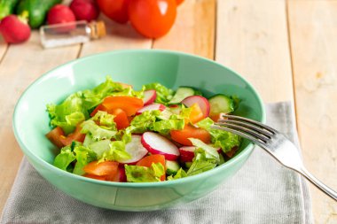Domatesli, salatalı ve turplu sebze salatası tarifi. Ahşap arka planda mevsimlik bir tabak. Diyet için vejetaryen yemeği.