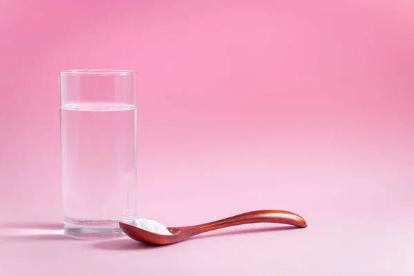 Natural bio supplement collagen powder in wooden spoon and glass of pure water on pink background. Concept healthy skin and bones, anti-aging extra protein product. Flatlay, place for text.