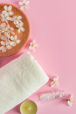Spa ve aromaterapi için kozmetik ürünler. Mumlar, deniz tuzu, havlu ve pembe arka planda çiçekler. Cilt bakımı ve güzellik anlayışı. Metnin için yer.