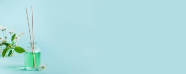 Aromatik difüzör ve mavi arka planda çiçekler. Spa ve rahatlama konsepti. Ev için güzel kokular. Mesajın için yer aç. Sancak biçimi