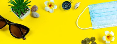 Koronavirüs salgını sırasında iyi yolculuklar. Yeni normal. Sarı arka planda tıbbi maske ve güneş gözlüğü. Flatlay, uzayı kopyala. Sancak biçimi