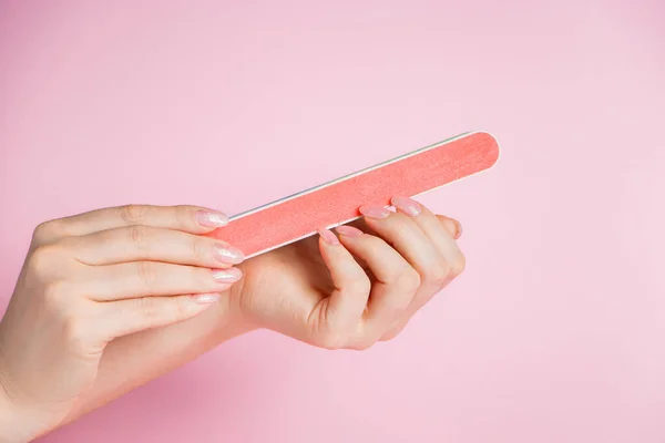 女人在家里修指甲 粉红背景上有指甲文件的手 — 图库照片