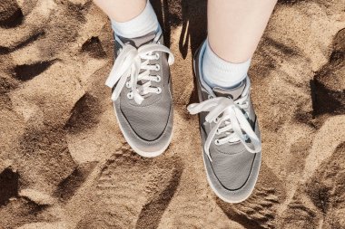 Kumsalda gri spor ayakkabılı bacaklar. Deniz kenarında yaz tatili konsepti. Yaşam tarzı seyahati. Pov manzaralı. Boşluğu kopyala.