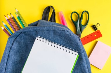 Sarı arka planda ofis malzemeleri olan okul çantası. Metin için yer.