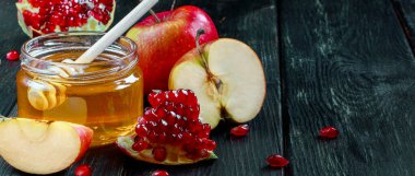 Rosh Hashanah kutlaması. Koyu ahşap bir arka planda bal, elma ve nar dolu kavanoz. Yahudi dini bayramı. Metin için yer, pankart biçimi.