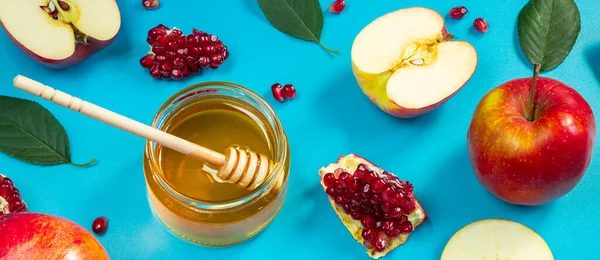 Pattern from apples, honey and pomegranates on a blue background. Happy Rosh Hashanah. Jewish religious holiday. Banner format.