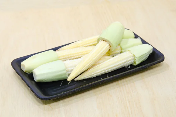 Baby corn fruit grouped on black plate on wooden board — Stock Photo, Image