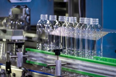 İçme suyu fabrikasındaki işlemleri tamamlamak için konveyör bandındaki PET şişeleri. Plastik şişe üretim sürecinin yüksek teknolojisi..