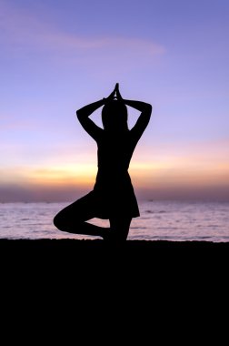 gün batımında sahilde Yoga uygulamak siluet genç kadın.