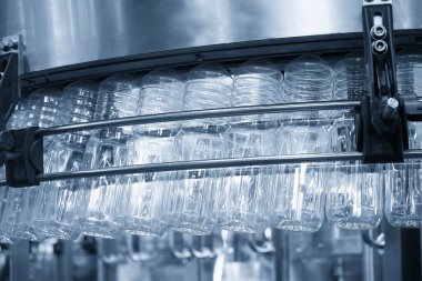 Açık mavi sahnedeki işlemleri tamamlamak için üstteki taşıma bandında asılı duran boş içme suyu şişeleri. İçme suyu üretim sürecinin yüksek teknolojisi. 