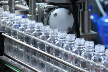 Mavi ton sahnesindeki otomatik içme suyu şişesi doldurma işlemi. Taşıma bandındaki içme suyunun seri üretimi. 