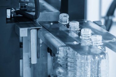 Konveyör bandındaki boş su şişeleri açık mavi sahnedeki üfleme makinesinden. İçme suyu üretim sürecinin yüksek teknolojisi. 