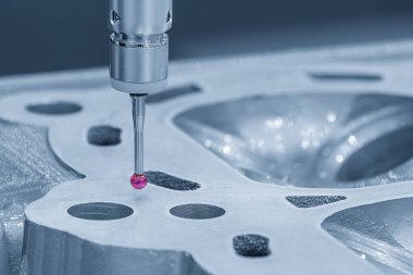 Açık mavi sahnede alüminyum silindir kafa parçalarını ölçen çok eksenli CMM makinesi. Çoklu eksen CMM makinesi ile otomotiv parçalarının kalite kontrolü.