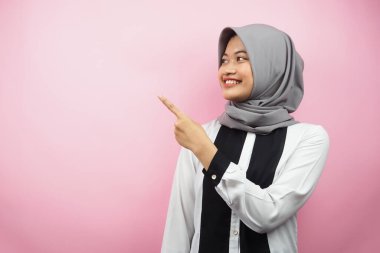 Güzel Asyalı genç Müslüman kadın elleri boş bir yeri işaret ediyor, gülümseyen, kendinden emin, coşkulu, neşeli, boş bir yere bakan, pembe arka planda izole edilmiş, reklam kavramı.