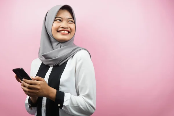 年轻美丽的亚裔穆斯林女子面带微笑 热情洋溢 手握智能手机 凝视着空旷的空间 呈现出某种东西 与粉色背景隔离 还有广告理念 — 图库照片