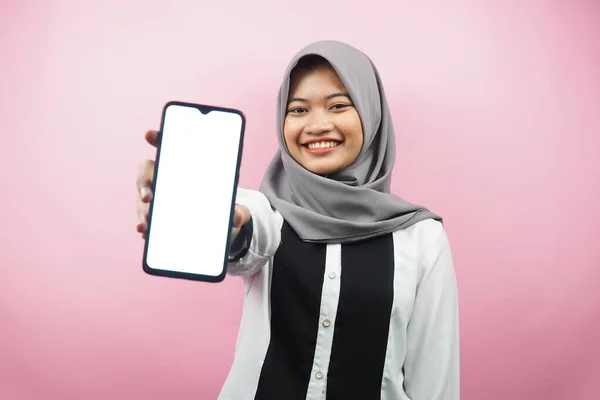 年轻美丽的亚裔穆斯林女子面带微笑 热情洋溢 手牵着智能手机 展示应用程序 展示某事 被粉色背景隔离 广告理念 — 图库照片