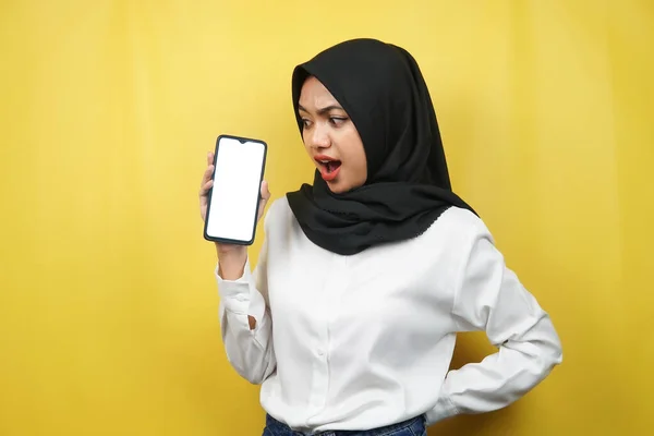美丽的年轻的亚裔穆斯林女子震惊 惊奇的表情 手持带有白色或空白屏幕的智能手机 推广应用程序 促销产品 展示某物 在黄色背景下被隔离 — 图库照片