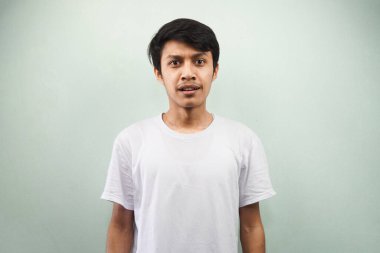 Beyaz tişört giyen Asyalı genç adam gri arka planda izole edilmiş kameraya bakıyor.