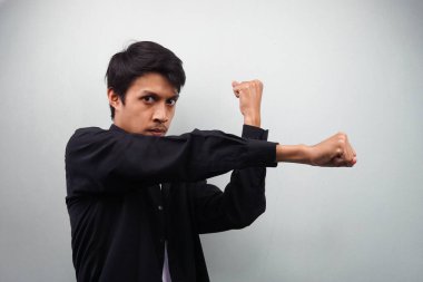 Siyah tişörtlü genç Asyalı ciddi ve güçlü dövüş sanatları eğitimi alıyor. Yumrukluyor, dövüşüyor, ruhuyla savaşıyor ve gri arka planda tek başına savaşmaya hazır.