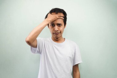 Beyaz tişört giyen Asyalı genç adam stresli, paniklemiş, kararsız, üzgün ve her şeyin yakında sona ermesini istiyor.