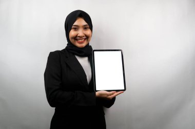 Güzel Asyalı genç Müslüman iş kadını kendine güvenen ve gülümseyen, beyaz ekranlı veya boş ekranlı tableti tutan, bir şey sunan, ürünü sunan, raporu sunan, gri arka planda izole edilmiş