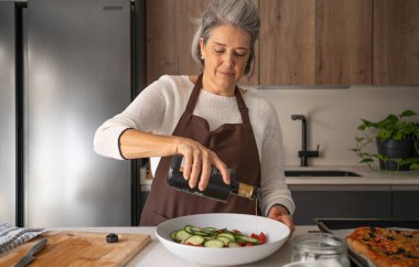 Yaşlı kadın taze bir salata hazırlıyor, mutfağına zeytinyağı döküyor.