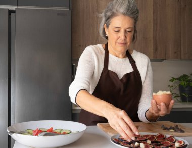 Önlüklü kadın sağlıklı bir yemek için dilimlenmiş incir ve peynir hazırlıyor.