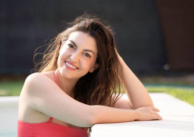 Esmer kadın gülümsüyor, açık havuzda serinletici suyun tadını çıkarıyor.