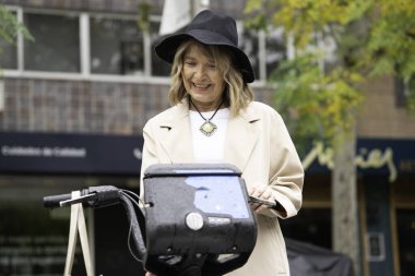 Gülümseyen son sınıf öğrencisi kadın, şehir ortamında akıllı telefonunu kullanarak ortak bir bisikleti etkinleştiriyor.