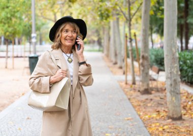 Bir sonbahar parkında yürürken telefonla konuşan son sınıf bir kadının portresi.