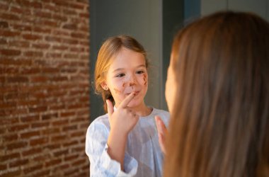 Mutfakta annesine gülümseyen çikolata lekeli küçük bir kız.