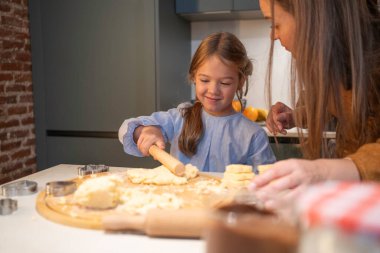 Kız, ev yapımı kurabiye pişirirken annesiyle mutlu mesut hamuru yuvarlıyor.