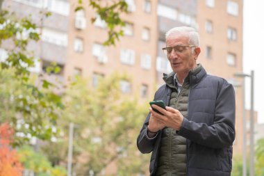 Kıdemli adam gülümsüyor, cep telefonunda fotokopi alanı ile mesajları kontrol ederken dışarı çıkıyor.