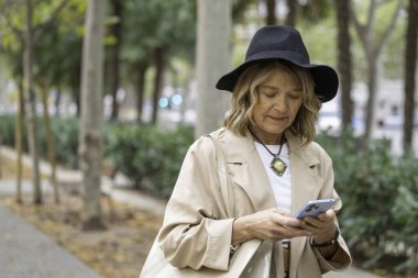 Üst düzey bir kadın sokakta akıllı telefonuyla şapka takıyor ve fotokopi odasıyla bağlantı kuruyor.