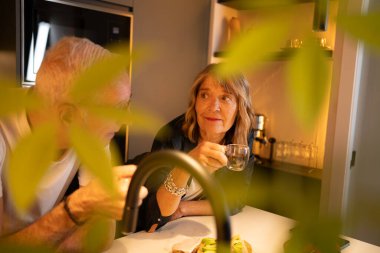 Modern mutfakta çay içerken rahatça sohbet eden olgun bir çift.