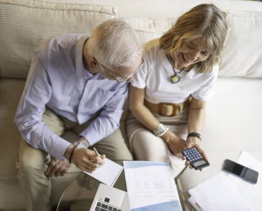 Üst düzey çift belgeleri analiz ediyor ve evdeki mali işleri yönetirken hesap makinesi kullanıyor.