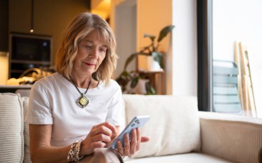Son sınıf öğrencisi kadın akıllı telefonuyla kayarken ve iletişim kurarken evdeki koltukta dinleniyor.